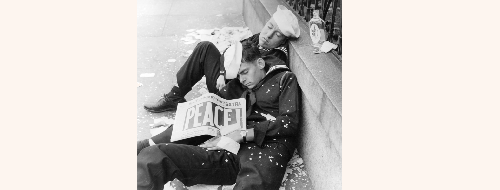 Photograph shows two sailors sleeping on the sidewalk. One of the sailors is holding the San Francisco Chronicle which reads PEACE! as the headline on its front page. San Francisco, California